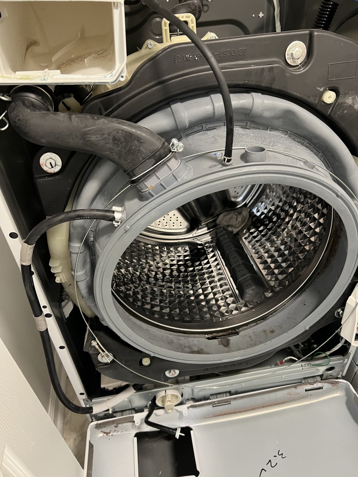 Front-load washer opened for service, with the drum, hoses and internal components visible.