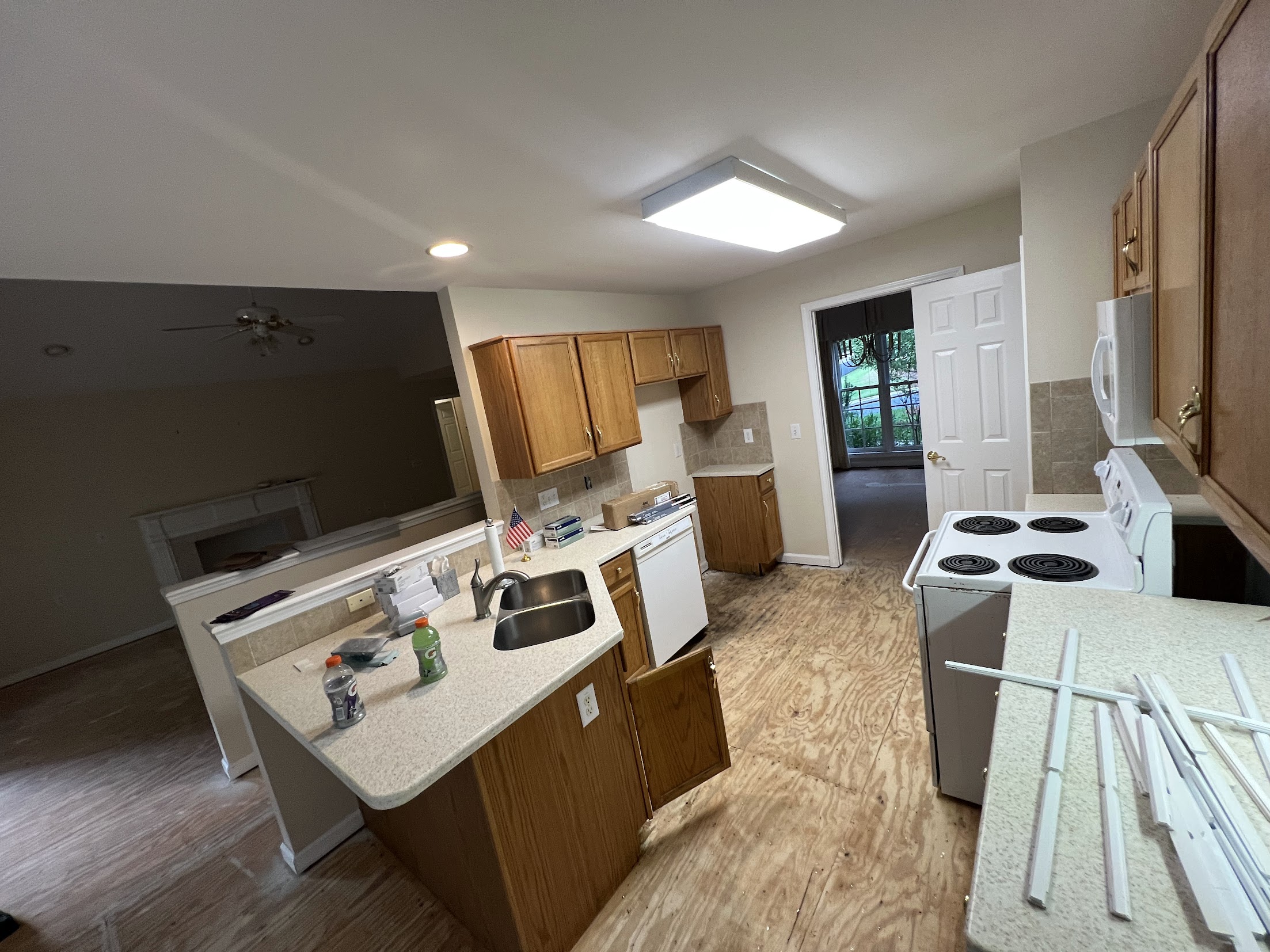 Kitchen before the update, with wood cabinets, light countertops, white appliances, and exposed subfloor