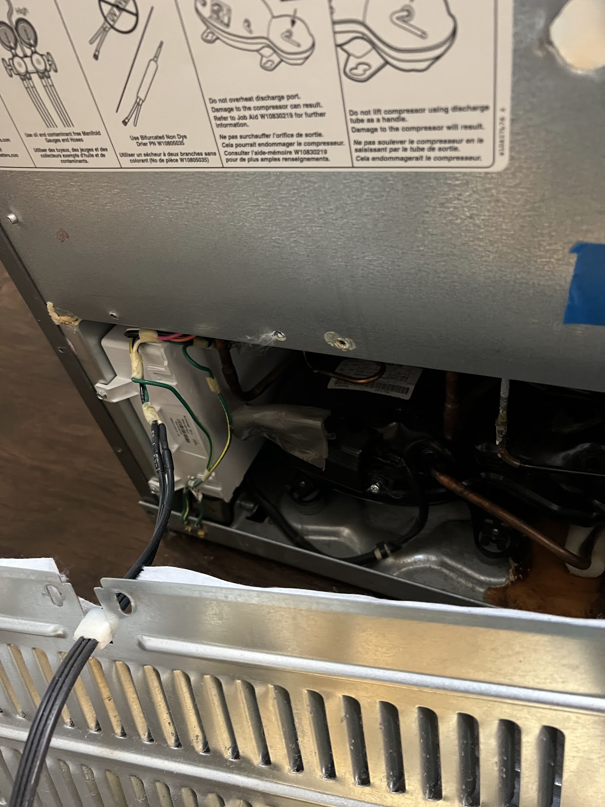 Rear access panel removed from a refrigerator for service, with the compressor and wiring visible