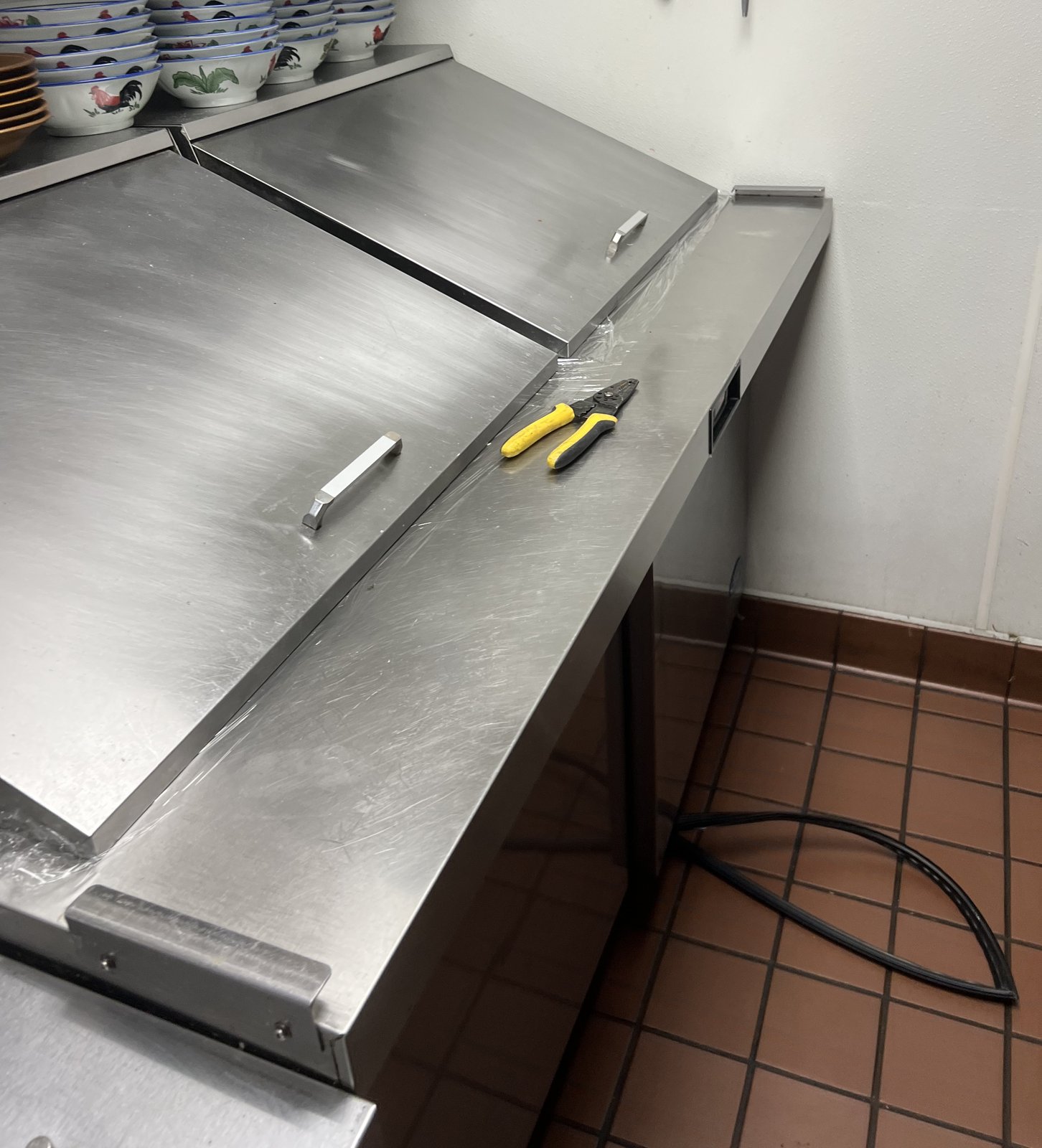 Stainless steel restaurant prep counter with lidded compartments and a service tool on the work surface.